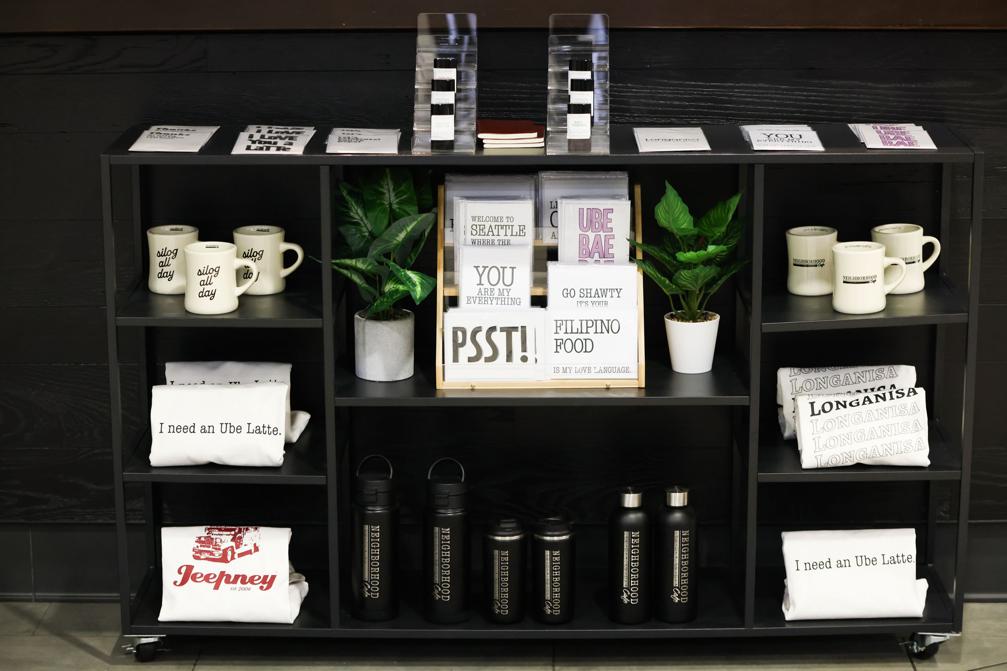 Neighborhood Cafe merchandise display with water bottles, mugs and attire